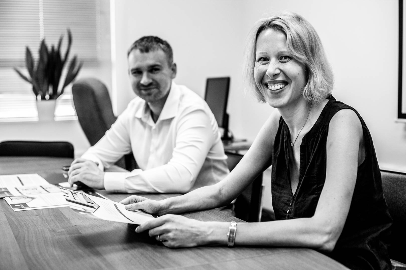Two World Courier associates, a woman and a man, smile while reviewing paperwork at a conference table.