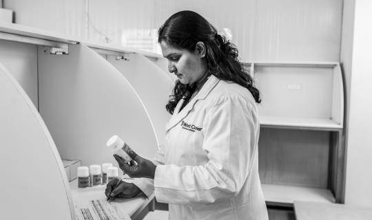 A woman in a lab coat examines a bottle of medication and takes notes.