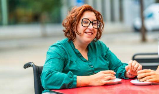 Women drinking coffee in wheelchair while smiling