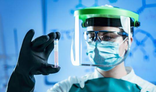 A scientist wearing a mask is examining a vial