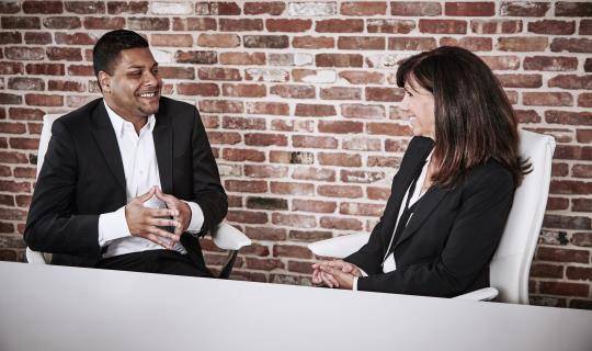 A man and a woman sit and talk at a conference table.