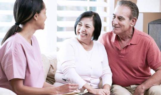 A visiting nurse talks to a man and a woman in their home.