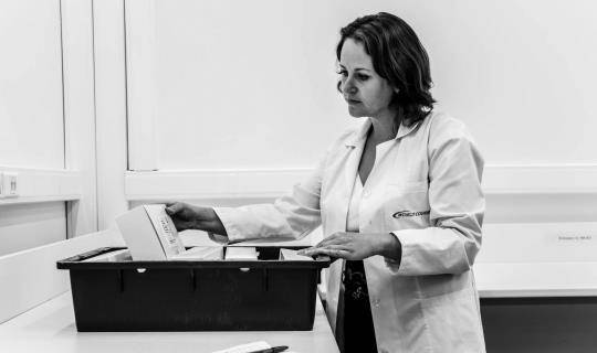 A woman in a lab coat looking at storage container with medication in it.