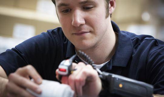 A man uses a handheld scanner to scan a barcode on a box of medication.