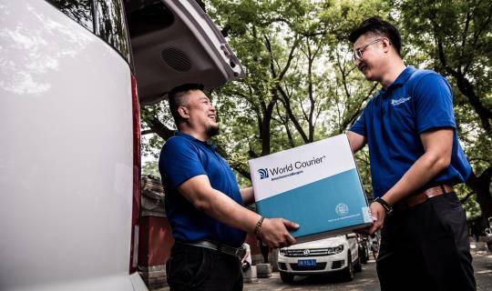 A World Courier driver passes a shipment from his van to another associate.