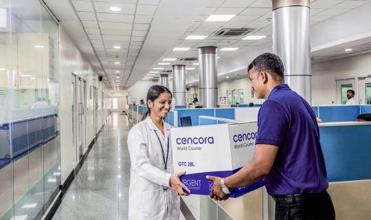 A World Courier associate delivers a shipment to a specialist in a lab coat inside a hospital