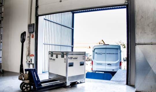 A shipping container is prepared to be loaded into a van at a loading dock.