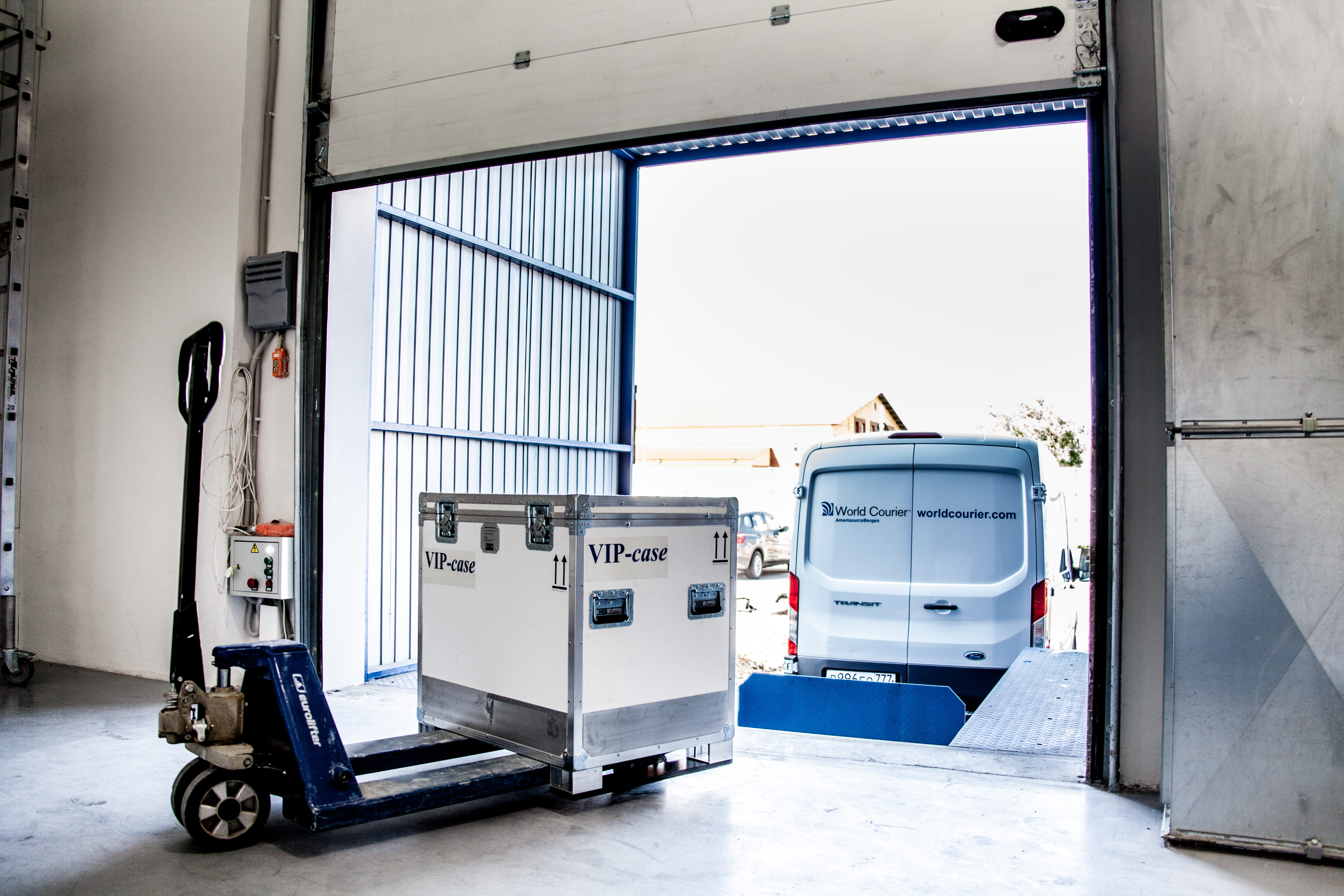 A shipping container is prepared to be loaded into a van at a loading dock.
