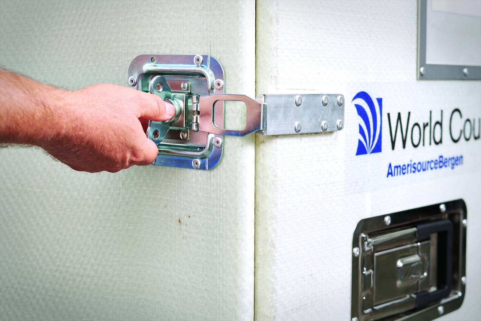 A hand reaches to unlatch a World Courier shipping container.