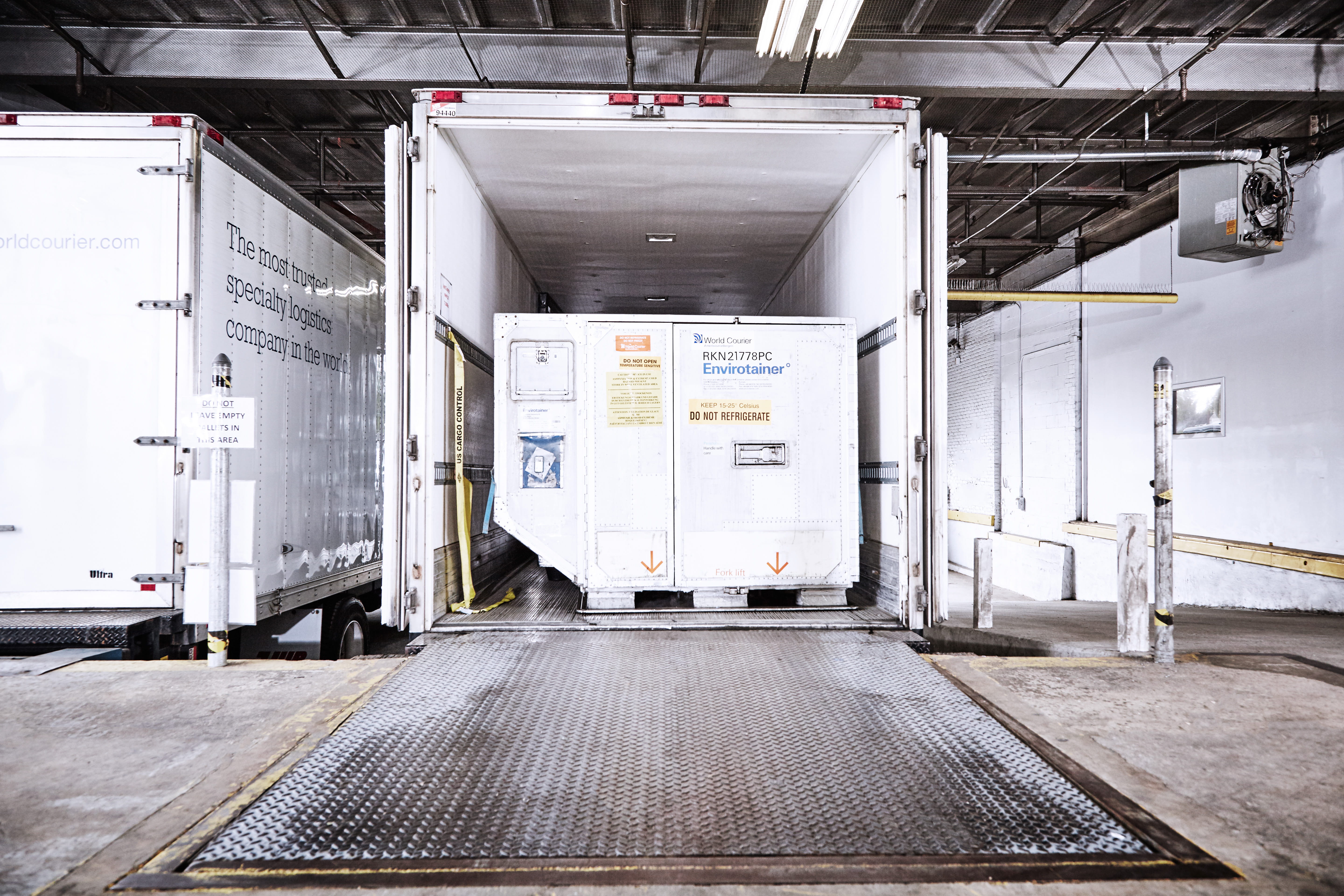 The back of a World Courier truck, or lorry, at a loading dock. An active shipping container sits inside.