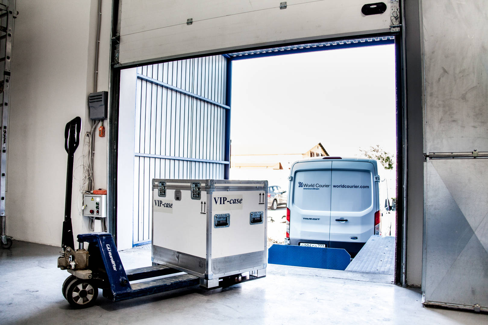 A shipping container is prepared to be loaded into a van at a loading dock.