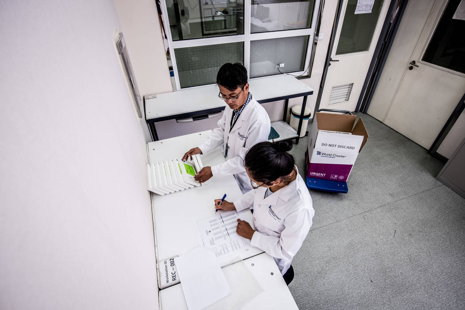 Male and female workers in lab coats checking a list.